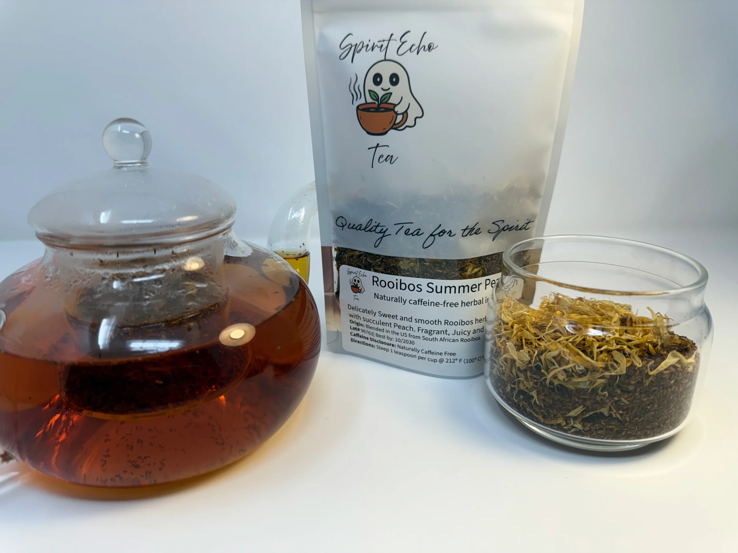 Tea-making setup with a teapot, tea packaging, and a jar of loose tea leaves on a white background.