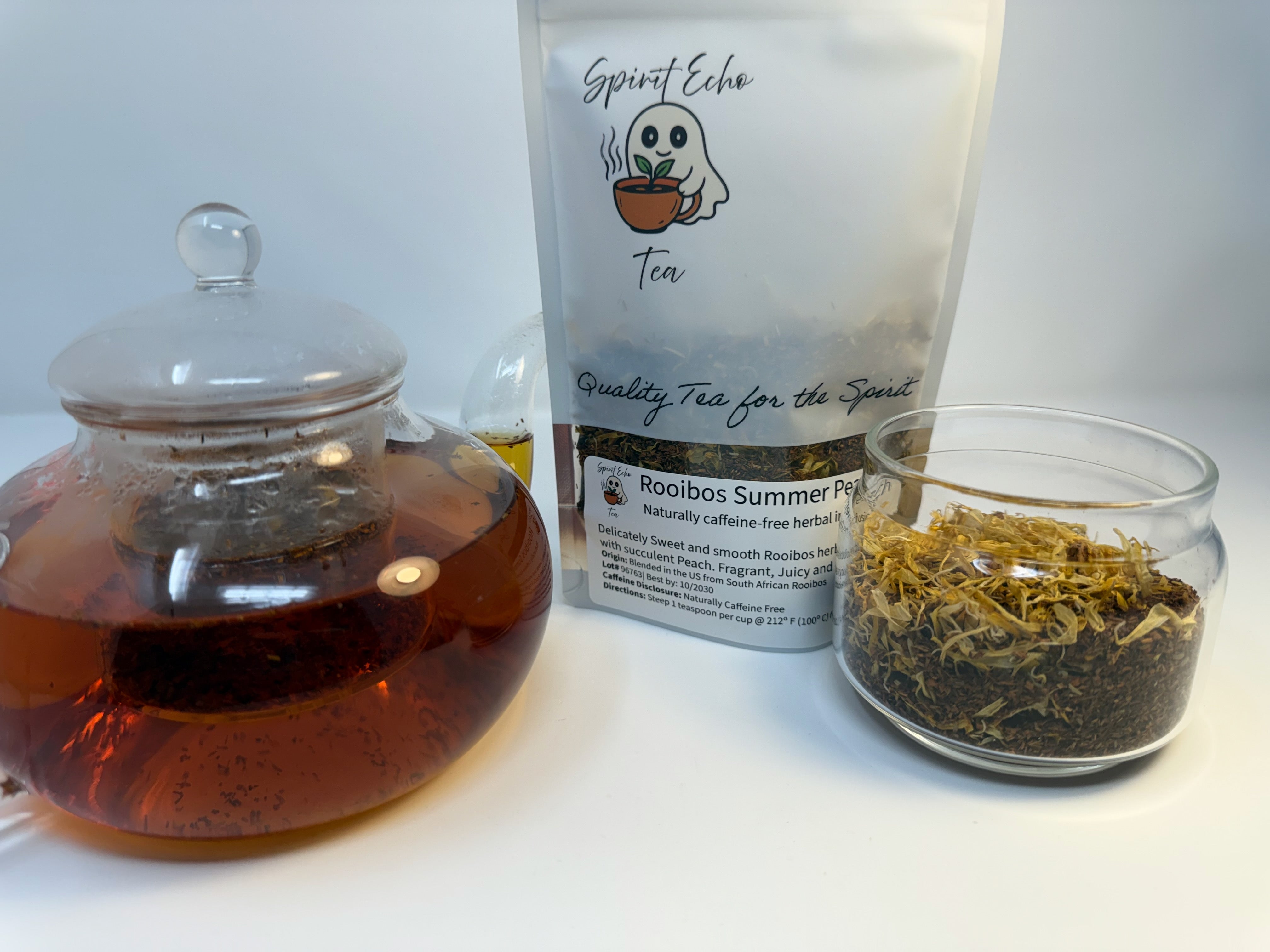 Tea-making setup with a teapot, tea packaging, and a jar of loose tea leaves on a white background.